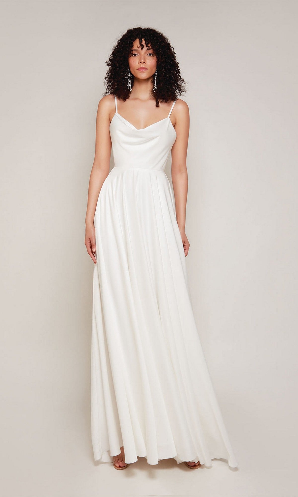 A woman wears the Alyce 7100 long formal dress in diamond white, featuring thin straps and a draped cowl neckline, standing against a plain light background.